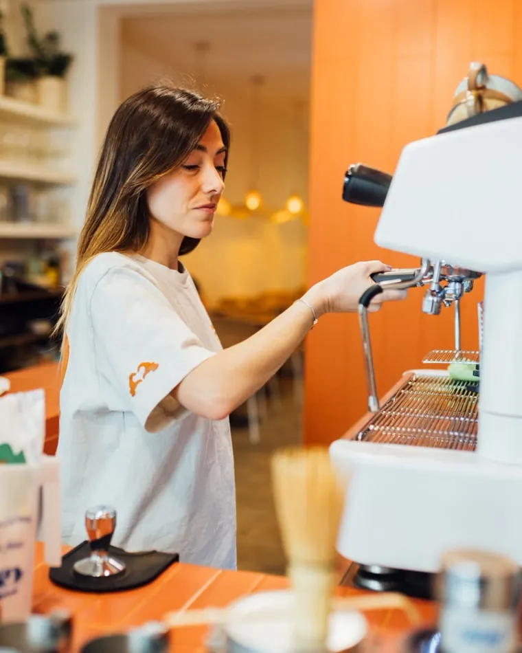Barista de ARAU preparando un espresso de especialidad en la máquina, con la pared de terracota de fondo